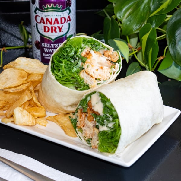 Vegan Caesar wrap with crispy chick'n, lettuce, and dressing, served with chips and a Canada Dry.